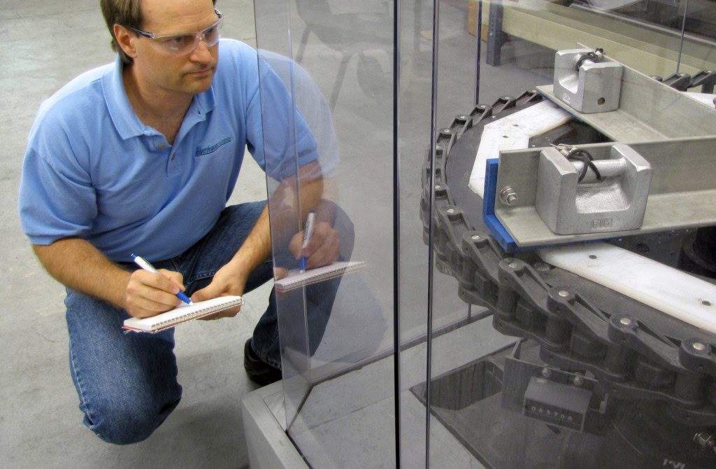 A man writing on a notepad next to a glass case that contains an industrial equipment.