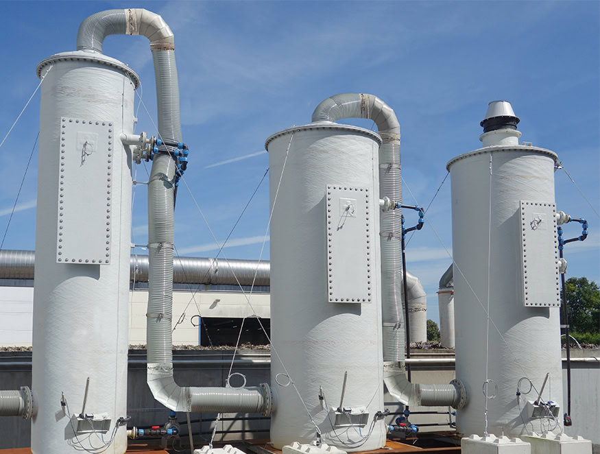 Industrial facility with three large, vertical cylindrical tanks. Each tank has attached pipes and valves, while the sky is visible in the background.