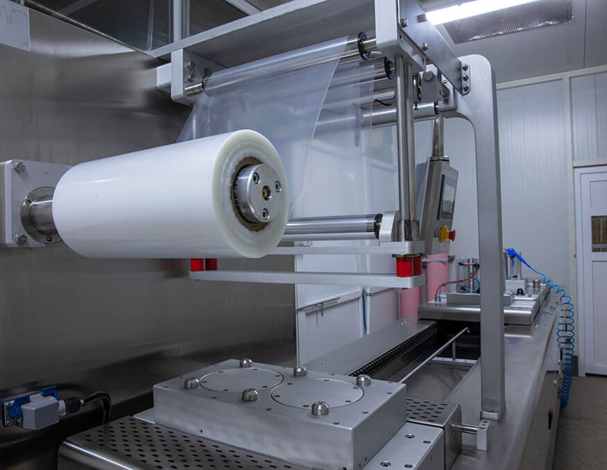 A modern packaging machine with a roll of plastic film installed, ready for use. Situated in a clean, industrial setting with stainless steel surfaces and control panels