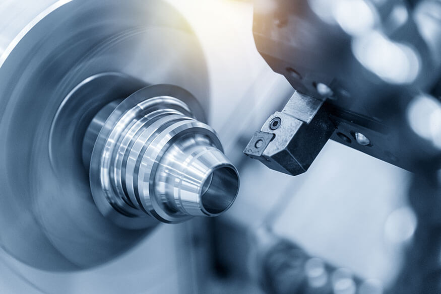 A close-up of a precision metal lathe machine in action, cutting a shiny metallic workpiece. The metal is cylindrical, and the lathe's cutting tool is making fine adjustments.