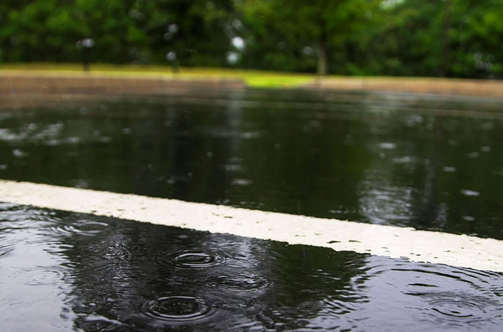 una carretera mojada con gotas de lluvia que crean ondas en el agua.
