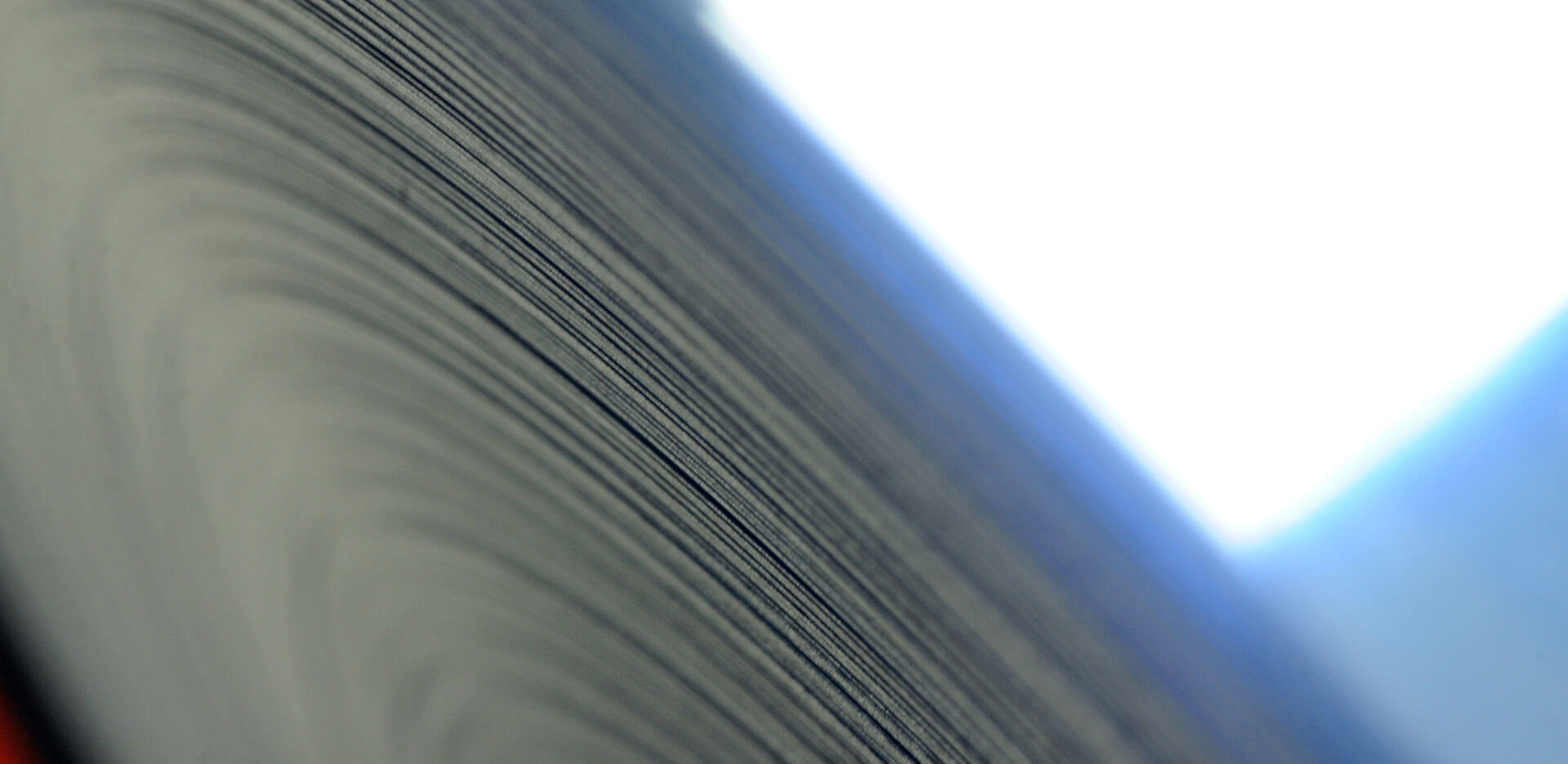 Primer plano del borde de una gran pila de papel o de un rollo de papel, con las hojas apretadas creando una serie de líneas curvas. La iluminación es suave, evocando una cálida sensación hogareña, con un tono azul a la izquierda y una luz más brillante y blanca a la derecha.